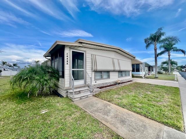 A single-story manufactured home features light-colored siding, a screened front entrance, and striped window awnings — 10920 INDEPENDENCE DRIVE, PORT RICHEY, FL