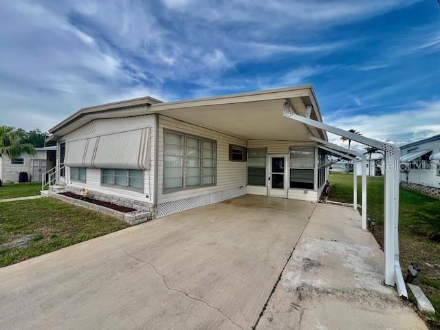 A single-story mobile home features a large attached carport and a concrete driveway — 10920 INDEPENDENCE DRIVE, PORT RICHEY, FL