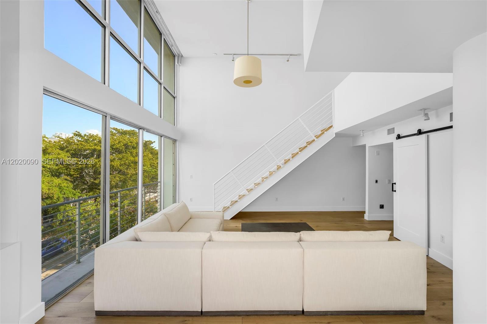 A modern living room features a large sectional sofa, floor-to-ceiling windows, and a staircase — 221 Jefferson Ave # 10, Miami Beach FL 33139, MIAMI BEACH, FL