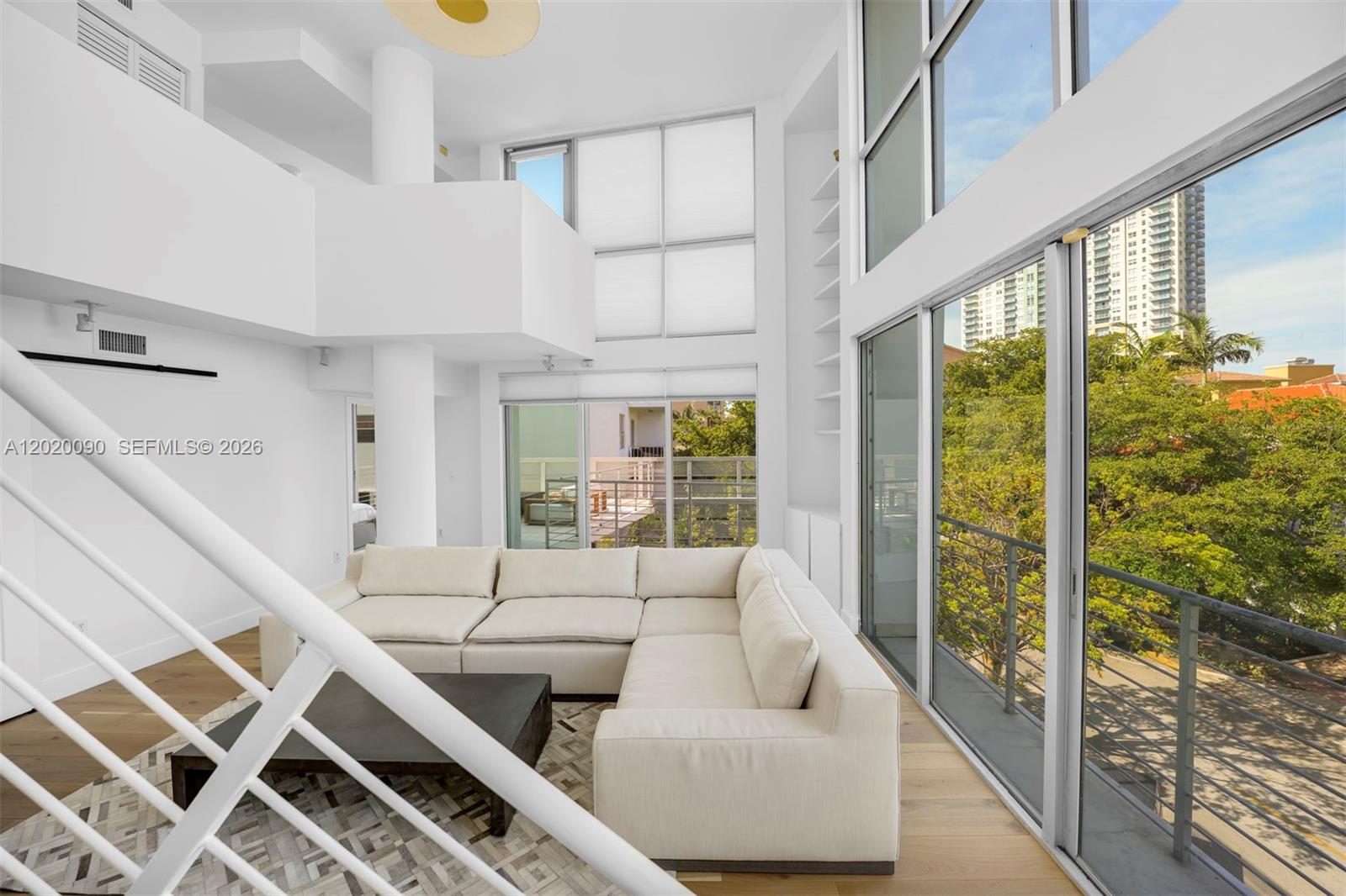 A modern, double-height living room features a white sectional sofa, hardwood floors, and floor-to-ceiling windows — 221 Jefferson Ave # 10, Miami Beach FL 33139, MIAMI BEACH, FL