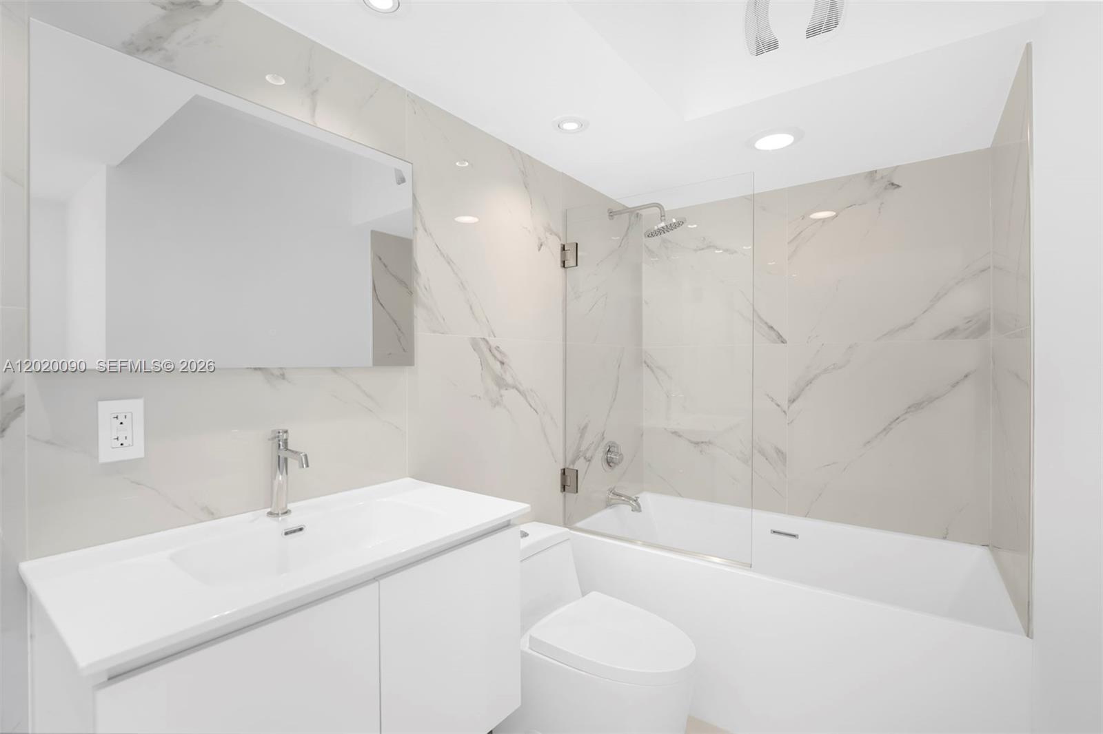 A modern bathroom features a white vanity, a toilet, and a bathtub with marble-look tiles — 221 Jefferson Ave # 10, Miami Beach FL 33139, MIAMI BEACH, FL