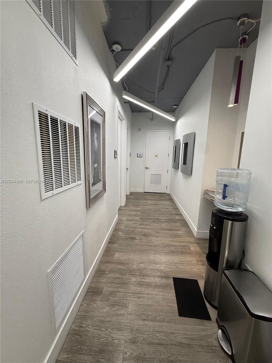 A hallway features wood-look flooring, white walls, exposed ceiling fixtures, and a water cooler — 2801 SW 3rd Ave, Miami FL 33129, MIAMI, FL