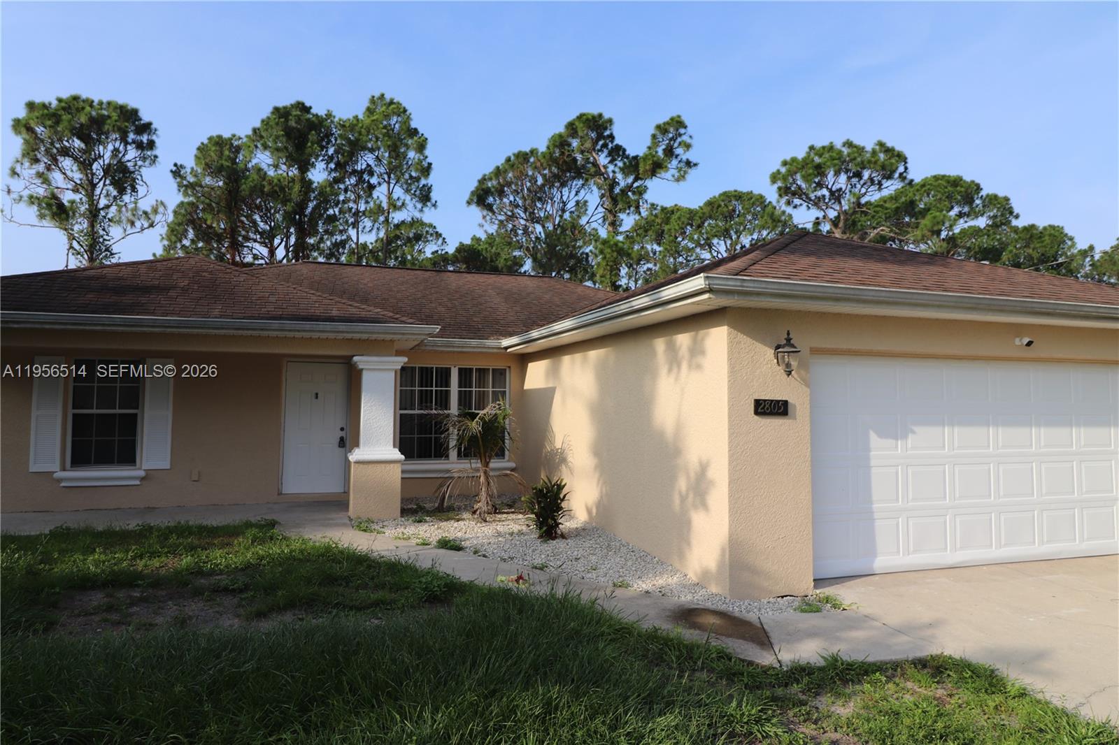 A single-story house with a beige stucco exterior, a white garage door, and a brown roof — 2805 1 sw st, Lehigh Acres FL 33972, LEHIGH ACRES, FL