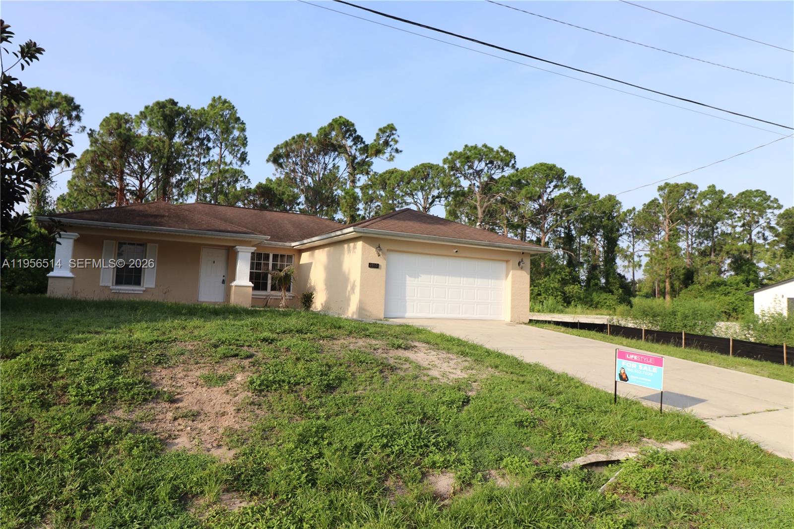 A single-story house with a beige exterior, a two-car garage, and a sloped grassy yard — 2805 1 sw st, Lehigh Acres FL 33972, LEHIGH ACRES, FL