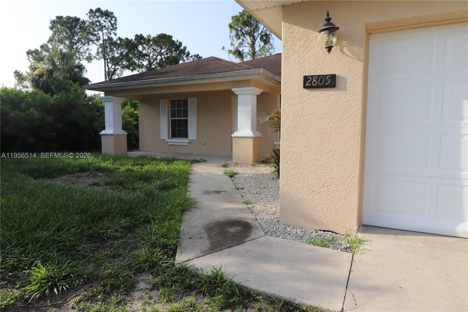 A tan house exterior features a concrete walkway, white columns, and a white garage door — 2805 1 sw st, Lehigh Acres FL 33972, LEHIGH ACRES, FL