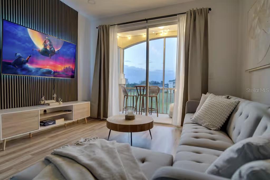 A living room features a wall-mounted television, a tufted sofa, and a balcony with seating — 8103 COCONUT PALM WAY UNIT 203, KISSIMMEE, FL