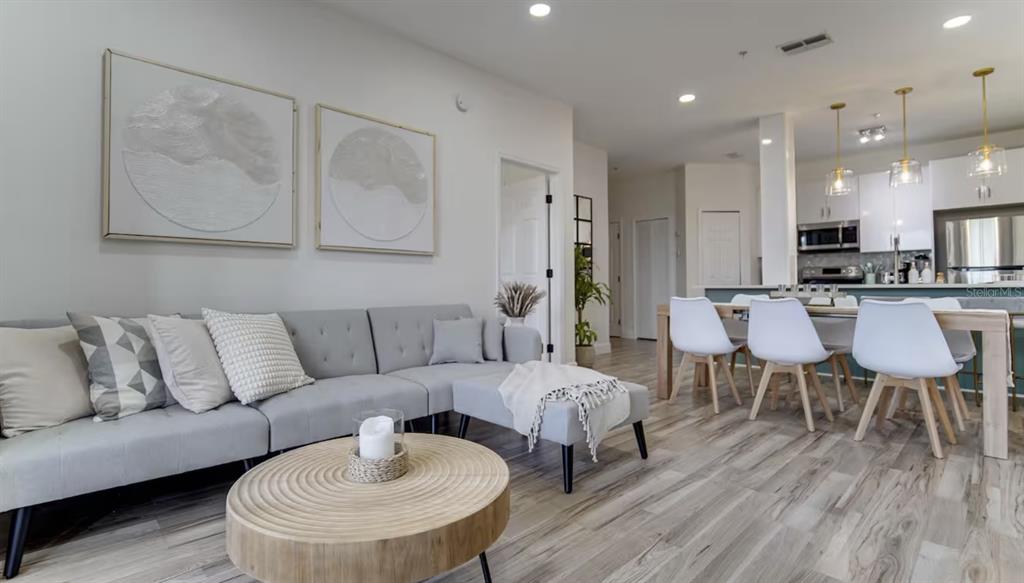 A living room with a gray sofa and wooden coffee table opens to a dining area — 8103 COCONUT PALM WAY UNIT 203, KISSIMMEE, FL