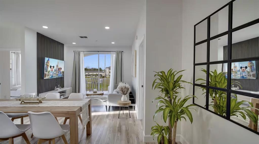A dining area and living room feature wood-look flooring, a paneled accent wall, and sliding doors — 8103 COCONUT PALM WAY UNIT 203, KISSIMMEE, FL