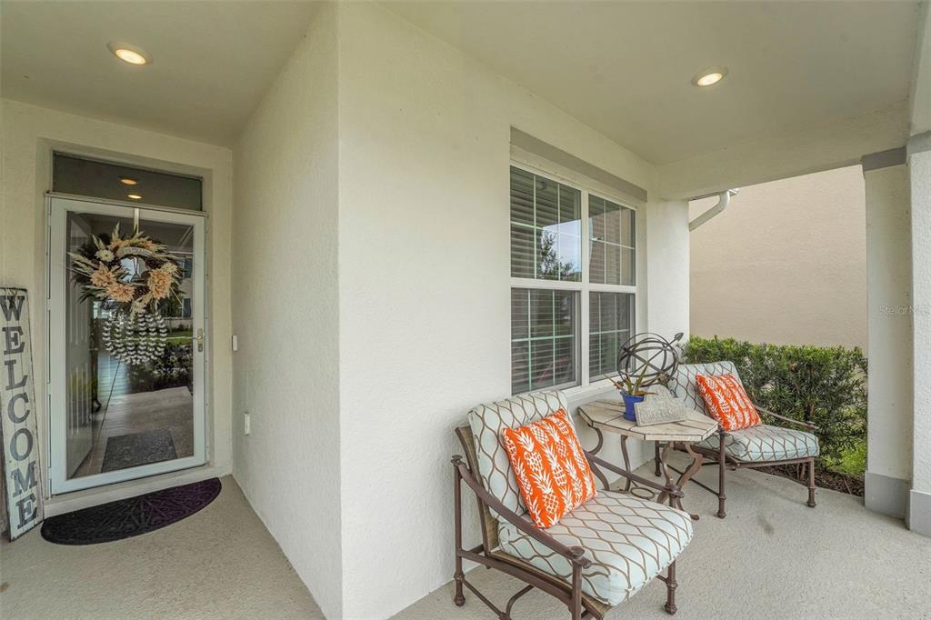 A covered front porch features a glass door, two chairs with patterned cushions, and a table — 1109 BRIMSTONE CIRCLE, WINTER HAVEN, FL