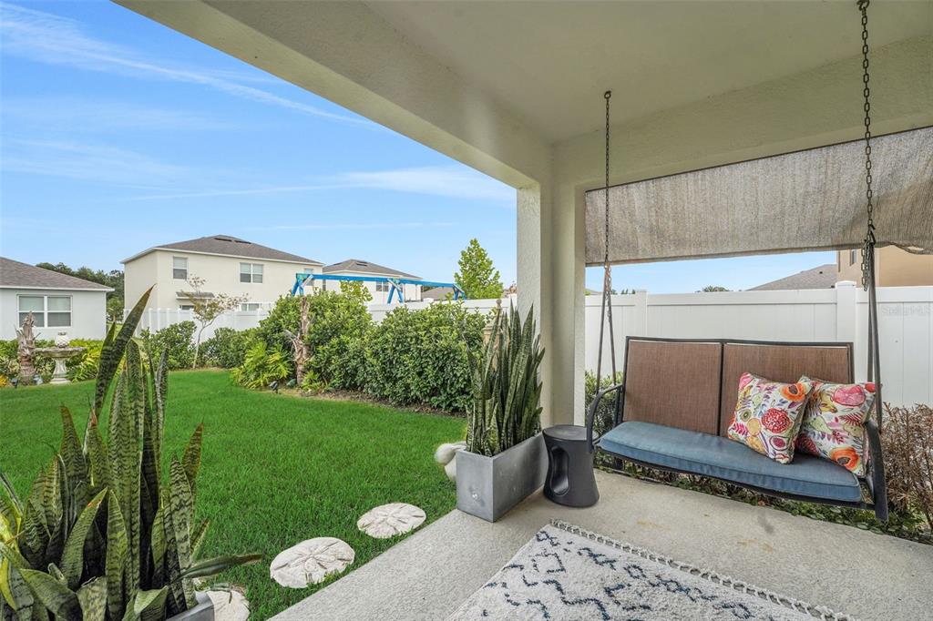 A covered patio features a hanging porch swing, potted snake plants, and a grassy backyard — 1109 BRIMSTONE CIRCLE, WINTER HAVEN, FL