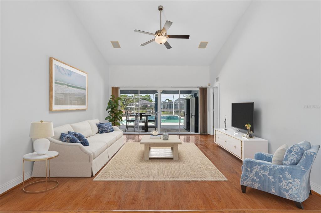 A living room with a vaulted ceiling, hardwood floors, and sliding doors opening to a pool — 20 CORONA COURT, PALM COAST, FL