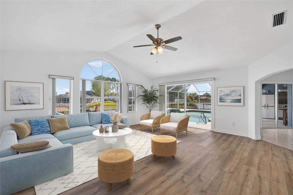 A bright living room features a blue sectional sofa, two rattan chairs, and a pool view — 20 CORONA COURT, PALM COAST, FL