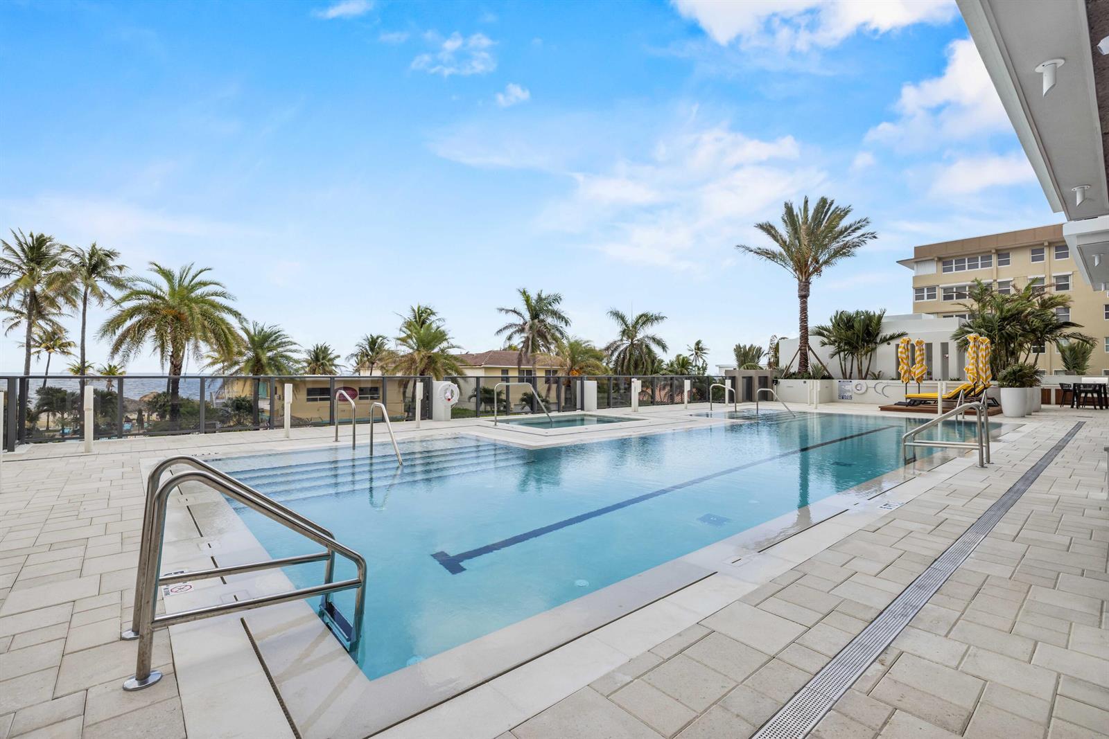 An outdoor swimming pool with a hot tub is surrounded by palm trees and pavers — 305 Briny Avenue # 301, Pompano Beach FL 33062, POMPANO BEACH, FL