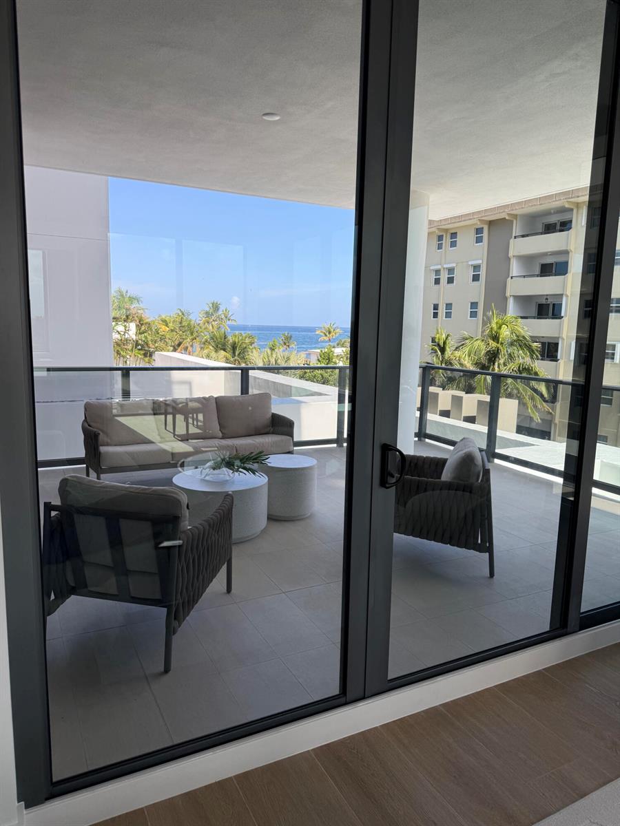 A balcony with outdoor furniture overlooks the ocean and a neighboring building through glass doors — 305 Briny Avenue # 301, Pompano Beach FL 33062, POMPANO BEACH, FL