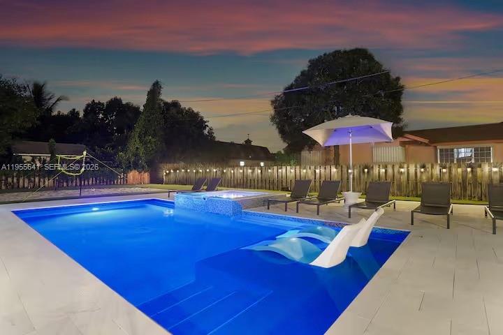 A backyard swimming pool with a sun shelf, lounge chairs, and a hot tub at dusk — 63 SE 5th Ave, Deerfield Beach FL 33441, DEERFIELD BEACH, FL