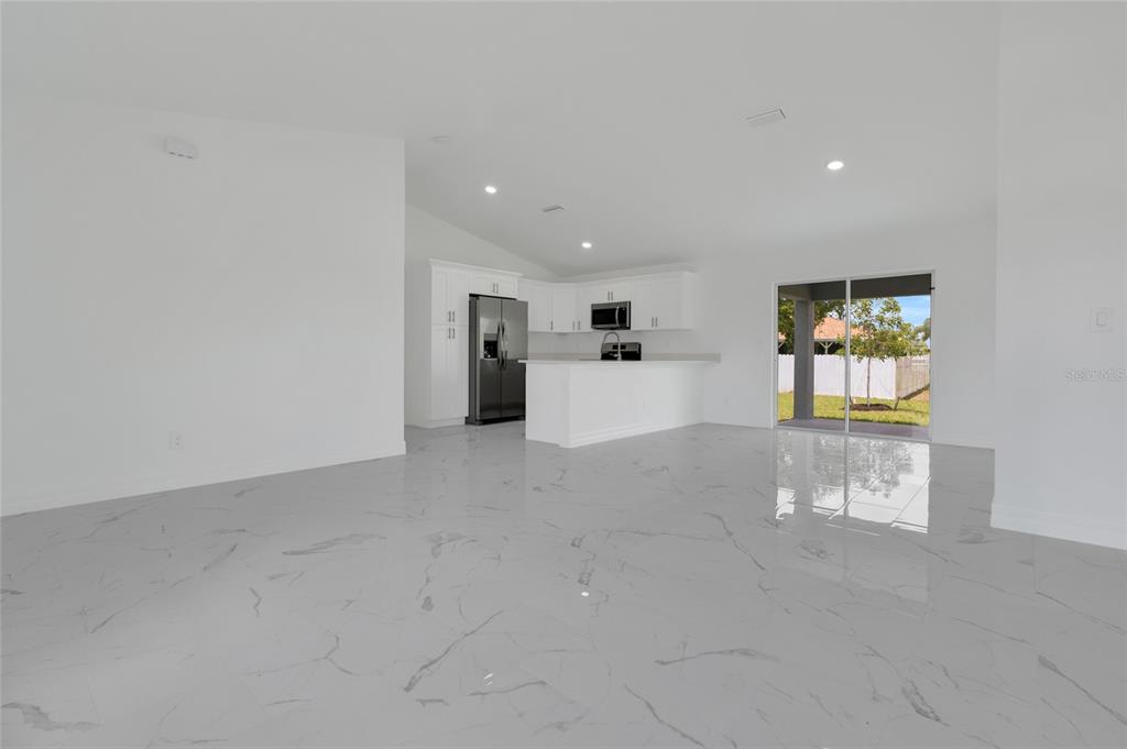 A bright, open-concept kitchen and living area features white cabinetry and polished marble-look tile flooring — 1808 NE 44TH STREET, CAPE CORAL, FL