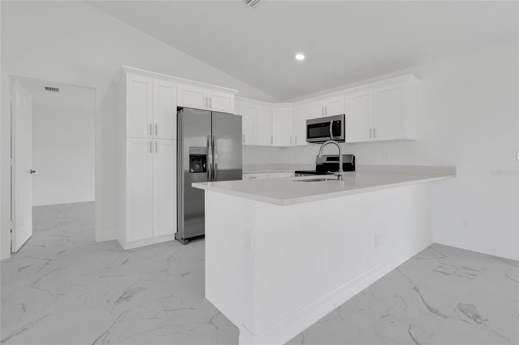 A modern kitchen features white cabinets, stainless steel appliances, and a quartz-topped island — 1808 NE 44TH STREET, CAPE CORAL, FL