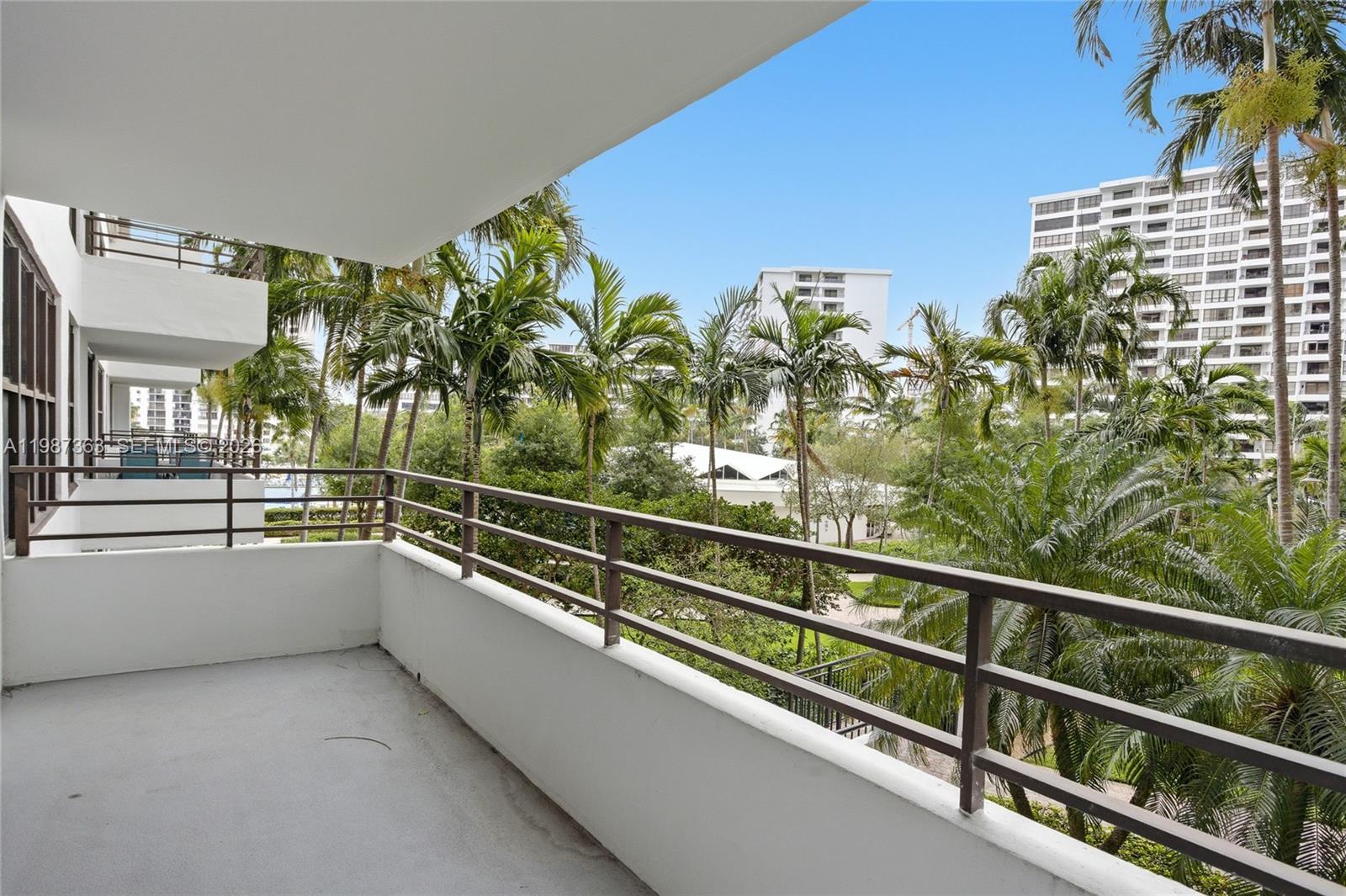 A balcony with a metal railing overlooks palm trees and nearby apartment buildings — 2500 Parkview Dr # 415, Hallandale Beach FL 33009, HALLANDALE BEACH, FL