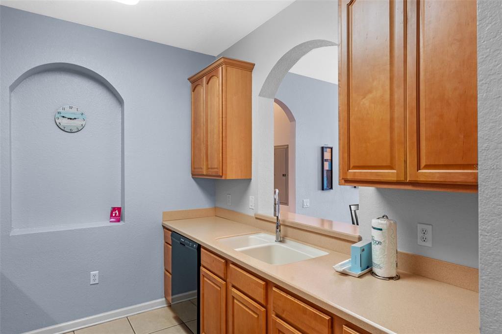 A kitchen features light wood cabinets, beige countertops, a double sink, and an arched wall niche — 4862 CAYVIEW AVENUE UNIT 407, ORLANDO, FL