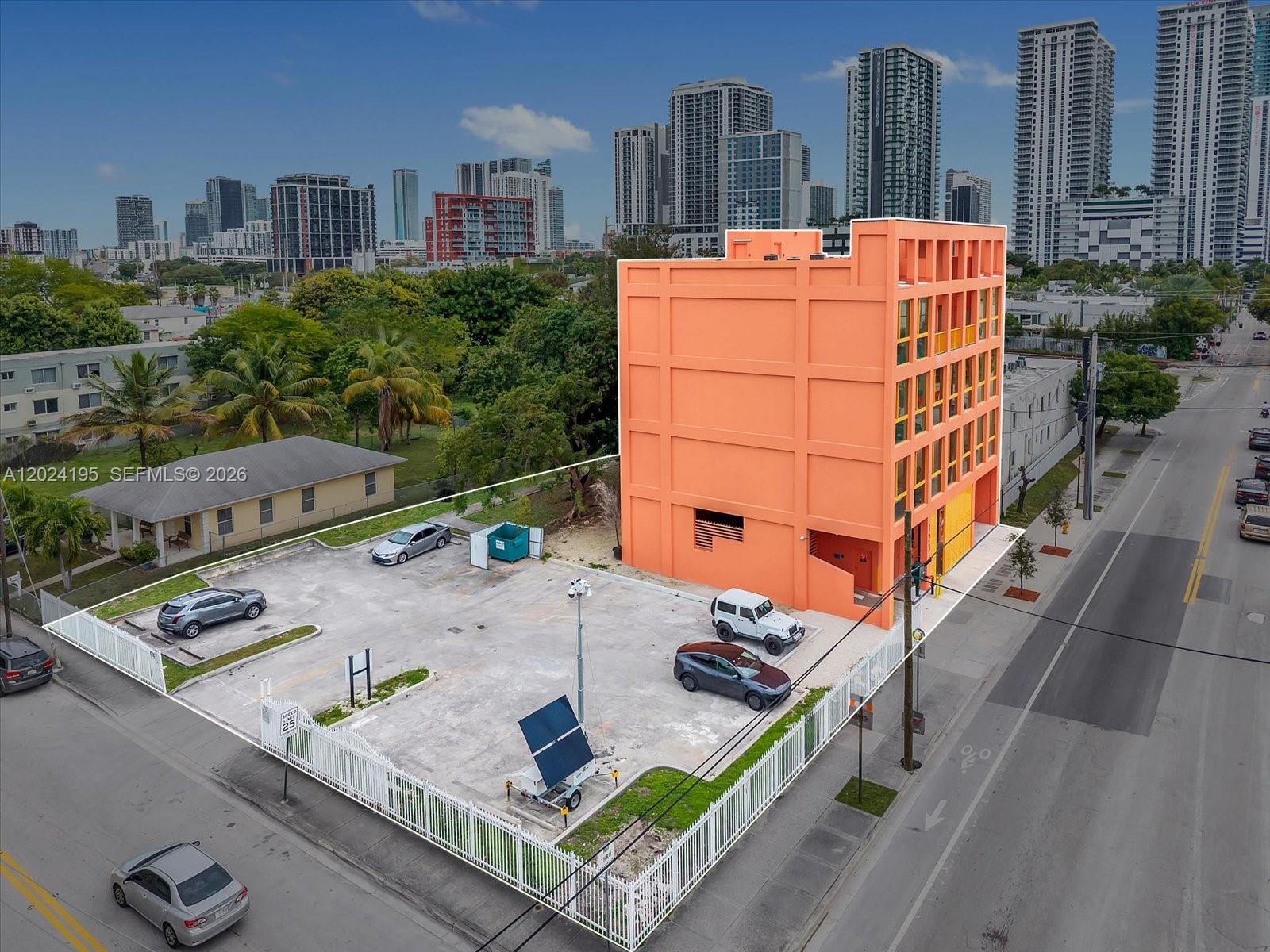 An aerial view shows a bright orange building with a fenced parking lot in front — 123 NW 14th St # 201, Miami FL 33136, MIAMI, FL