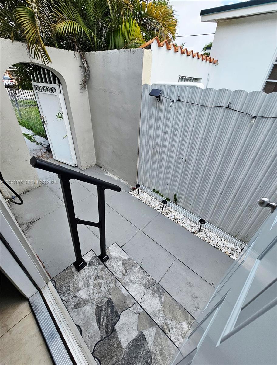 An outdoor entryway features a stone-tiled step, a black metal handrail, and a corrugated fence — 000 NW 51 AVE, Miami FL 33126, MIAMI, FL
