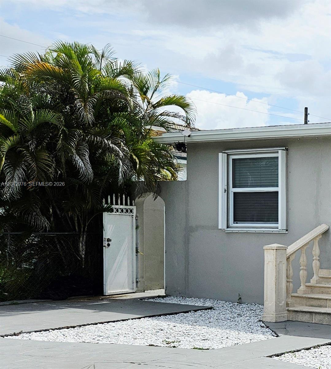 A white gate stands next to a gray house with a window and stone stairs — 000 NW 51 AVE, Miami FL 33126, MIAMI, FL