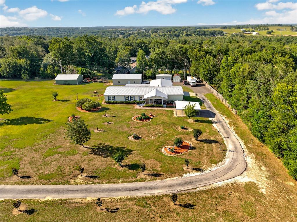 An aerial view shows a white house with a metal roof surrounded by grassy land — 9706 US HIGHWAY 301, DADE CITY, FL