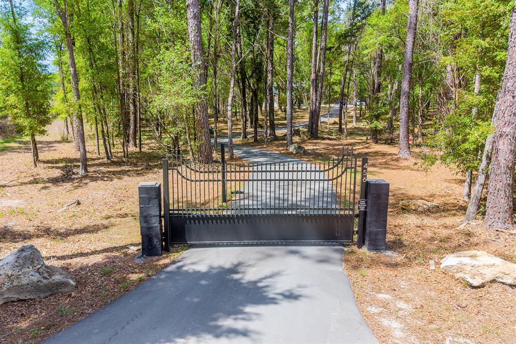 A black metal security gate spans a paved driveway leading into a wooded residential property — 456 SW BRADENTON WAY, FORT WHITE, FL