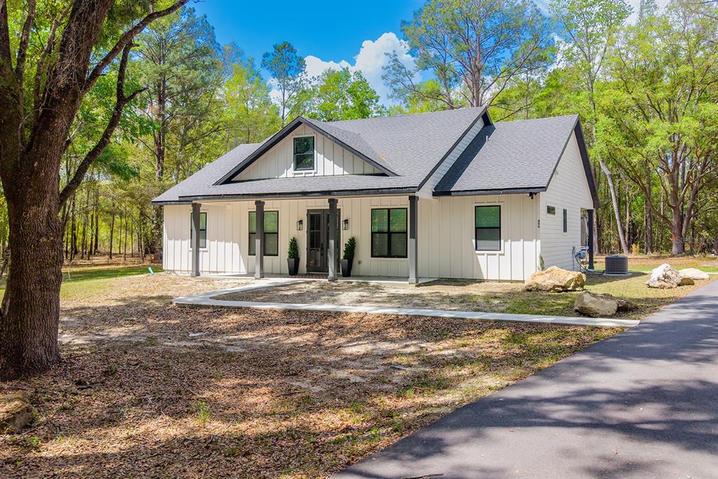 A white farmhouse-style home with a dark roof and porch sits in a wooded lot — 456 SW BRADENTON WAY, FORT WHITE, FL