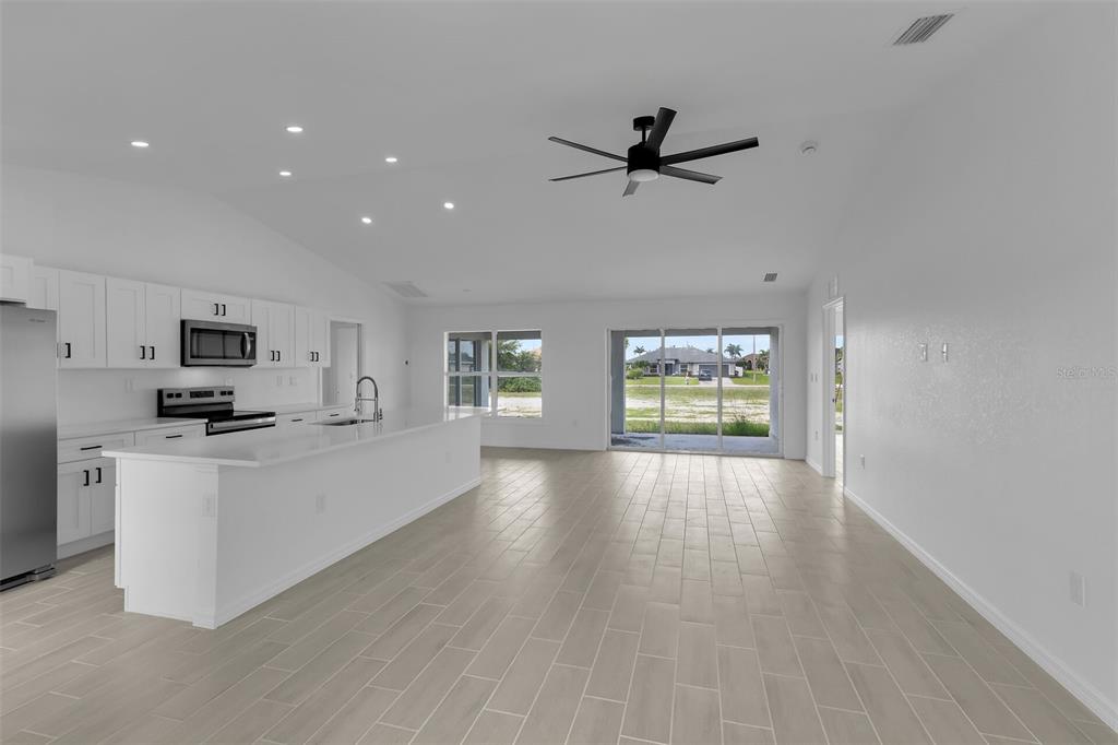 A bright, open-concept kitchen and living area features white cabinetry, stainless appliances, and tile flooring — 4130 NW 33RD STREET, CAPE CORAL, FL