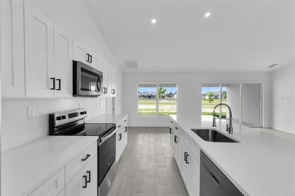 A modern kitchen features white cabinets, stainless steel appliances, a large island, and tile flooring — 4130 NW 33RD STREET, CAPE CORAL, FL