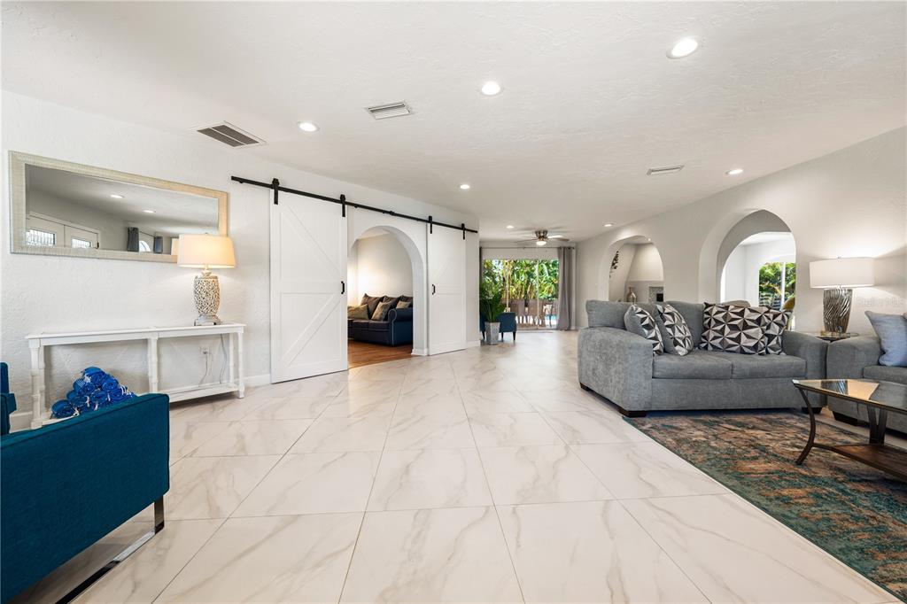 A bright living room features white tile floors, arched doorways, and a sliding barn door — 3524 S SCHOOL AVENUE, SARASOTA, FL