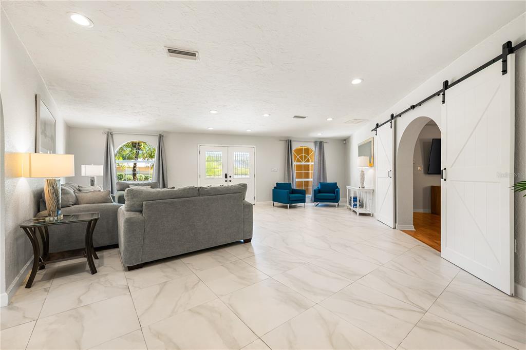 A spacious living room features light tile flooring, gray sofas, blue armchairs, and white barn doors — 3524 S SCHOOL AVENUE, SARASOTA, FL