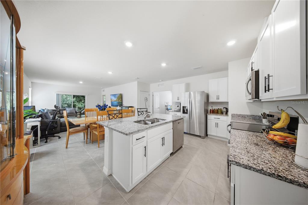A kitchen with white cabinets, granite countertops, and a center island opens to a dining area — 479 PELHAM PARK DRIVE, DELAND, FL