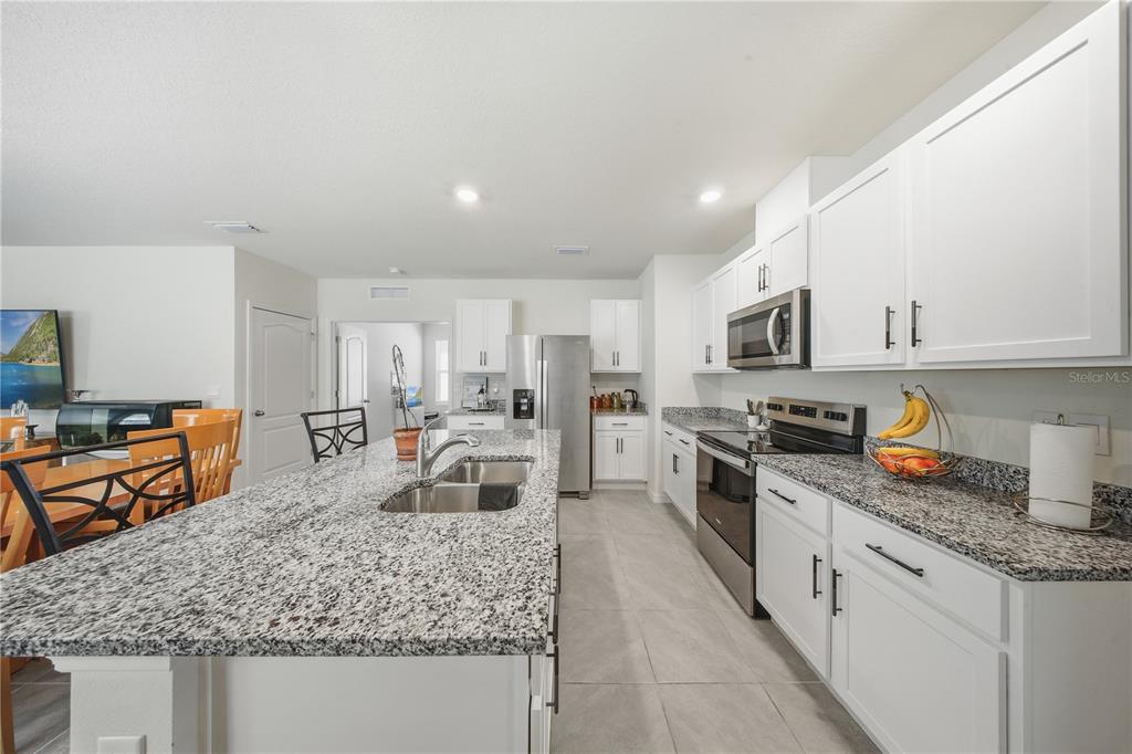 A kitchen features white cabinets, granite countertops, stainless steel appliances, and a large center island — 479 PELHAM PARK DRIVE, DELAND, FL