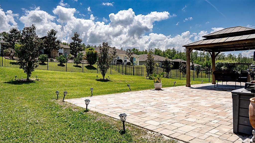 A backyard features a paved patio, a gazebo, and a metal fence under a cloudy sky — 5526 LIMESTONE STREET, MOUNT DORA, FL
