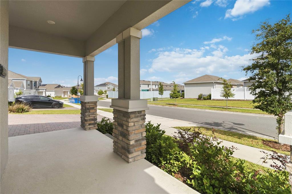A covered front porch with stone-based pillars overlooks a suburban street and neighboring houses — 3000 ELLA WAY, ST CLOUD, FL