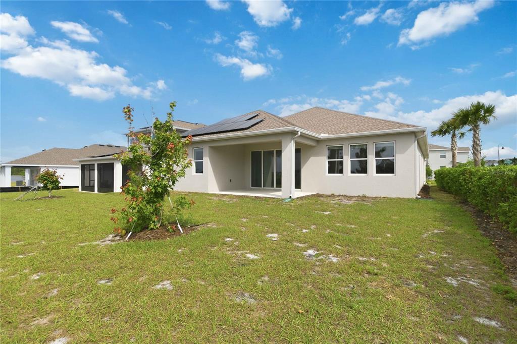 The exterior rear view of a single-story house features a covered patio and solar panels — 3000 ELLA WAY, ST CLOUD, FL