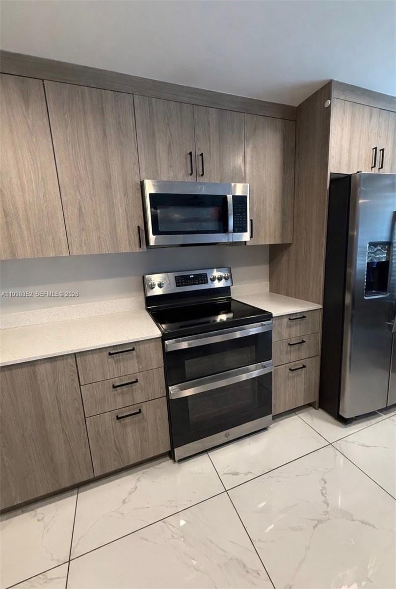 A living room with a television and kitchen island featuring light wood cabinets and tile flooring — 25761 SW 144th Ave, Homestead FL 33032, HOMESTEAD, FL