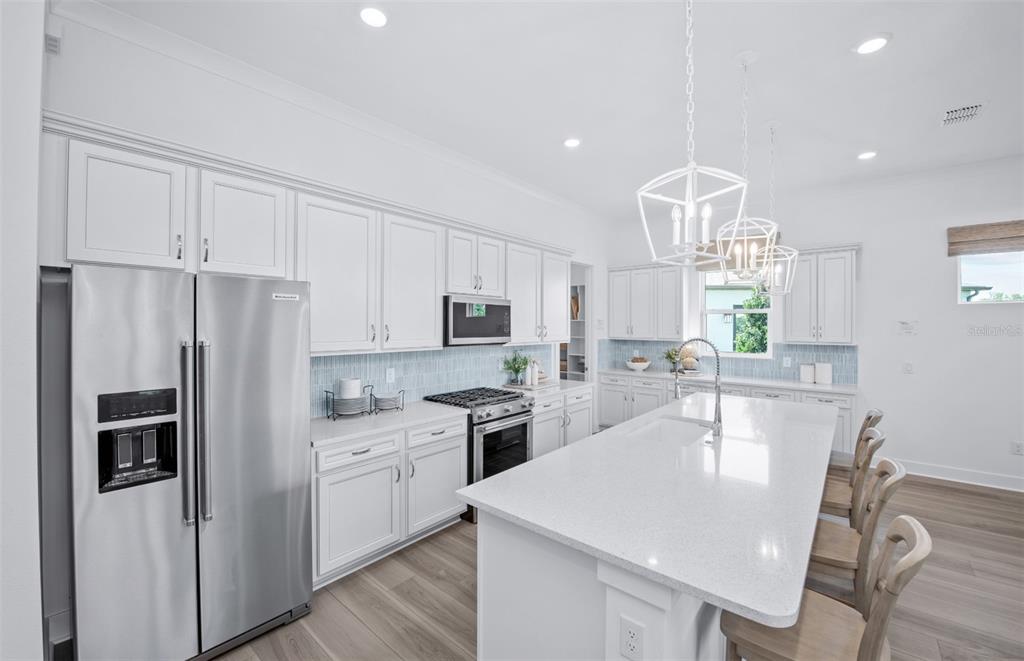 A bright kitchen features white cabinetry, stainless steel appliances, a large island, and light flooring — 5764 SW 82ND TERRACE ROAD, OCALA, FL