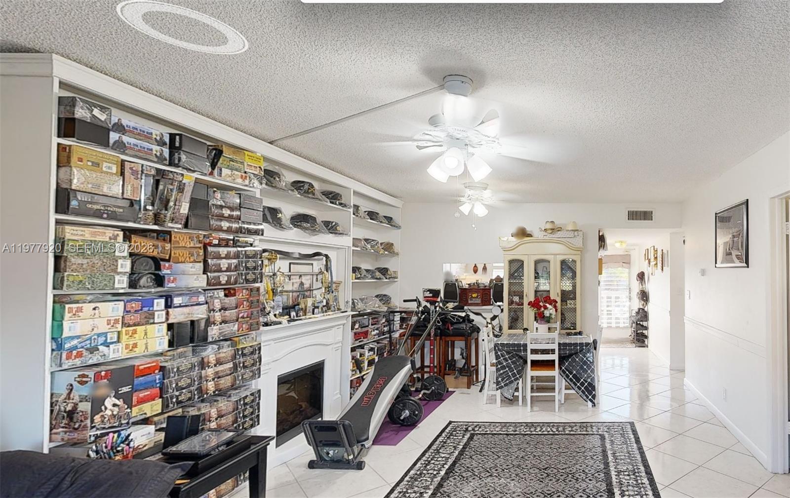 A living room features a fireplace, extensive shelving filled with collectibles, and a dining area — 6570 Royal Palm Blvd # 215J, Margate FL 33063, MARGATE, FL