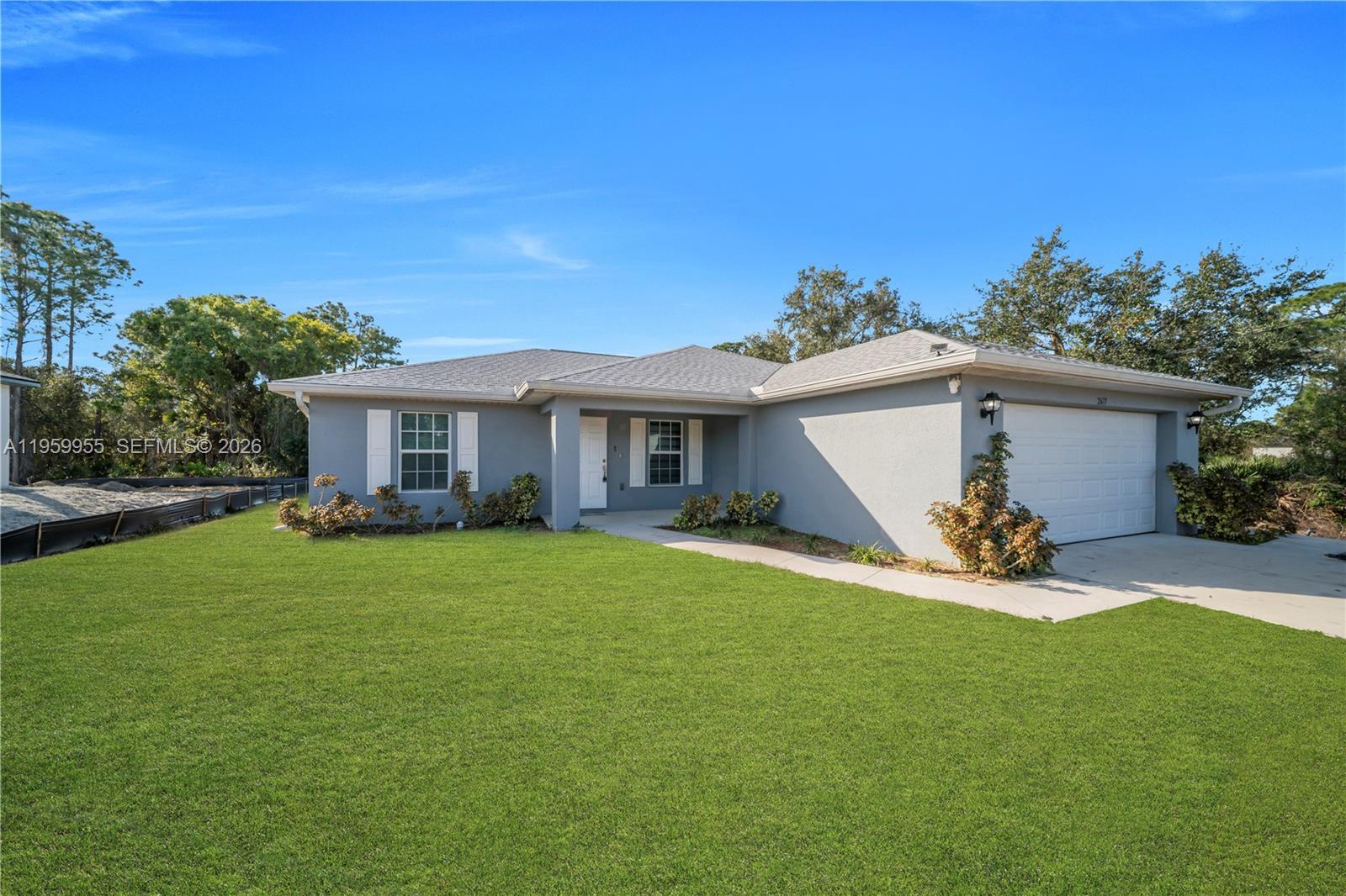 A single-story gray house features a white garage door, white shutters, and a green lawn — 2617 53rd ST W, Lehigh Acres FL 33971, LEHIGH ACRES, FL