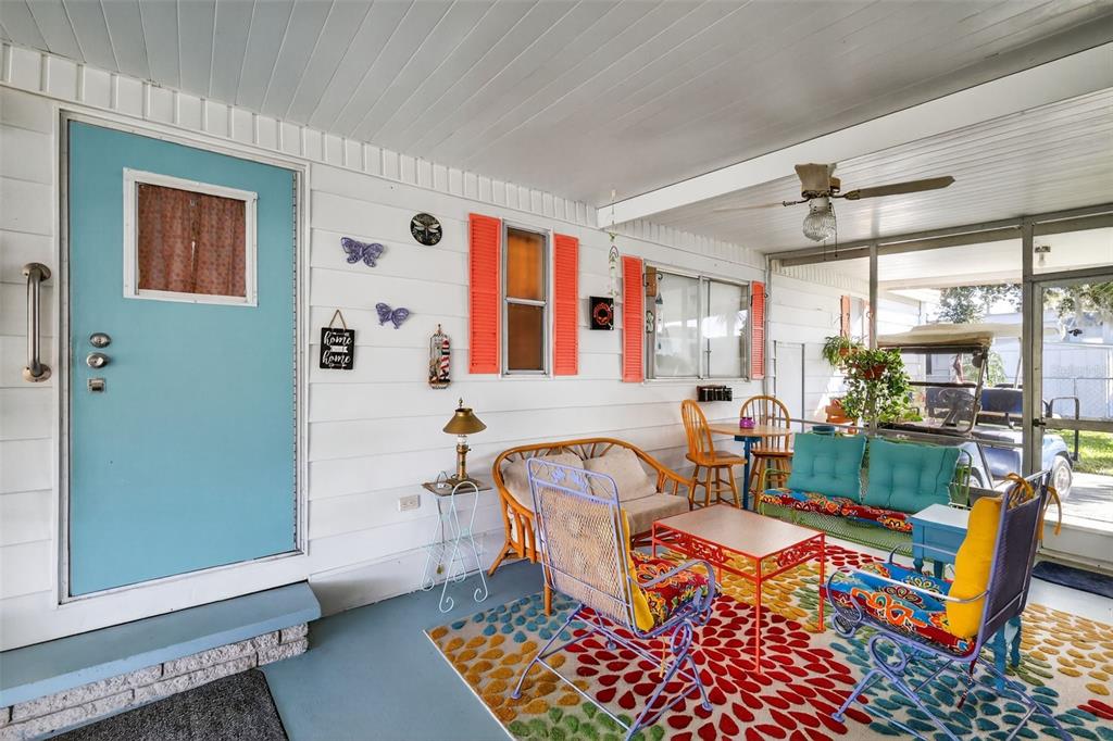 A covered porch features a blue door, colorful outdoor furniture, and a patterned area rug — 11600 MAGNOLIA AVENUE, TAVARES, FL
