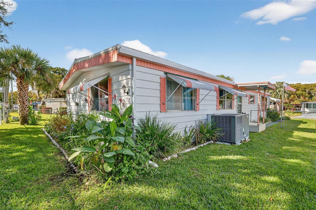 A single-story mobile home with light siding, orange trim, and awnings sits on a grassy lot — 11600 MAGNOLIA AVENUE, TAVARES, FL