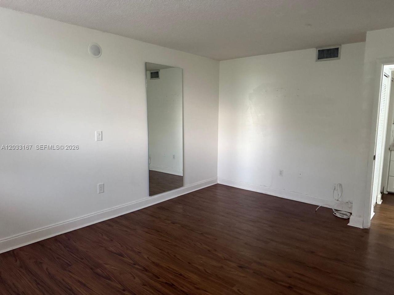 An empty room features white walls, a floor-to-ceiling wall mirror, and dark wood-look flooring — 8305 SW 152nd Ave # 409, Miami FL 33193, MIAMI, FL