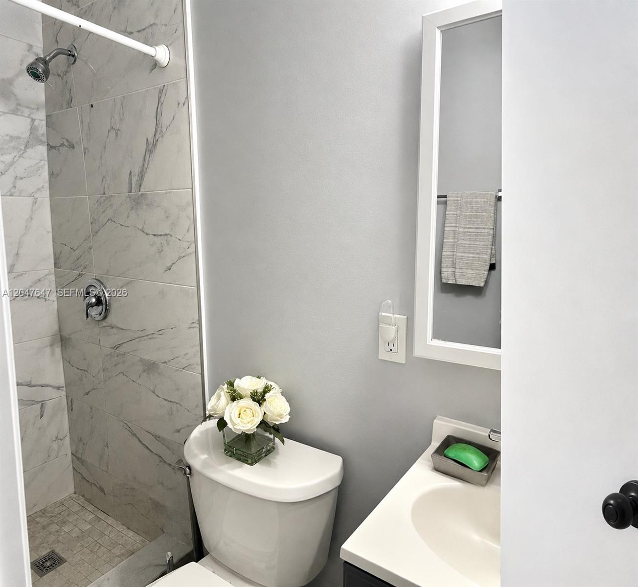 A small bathroom features a marble-tiled shower, a white toilet, and a vanity sink — 525 E 24th St, Hialeah FL 33013, HIALEAH, FL