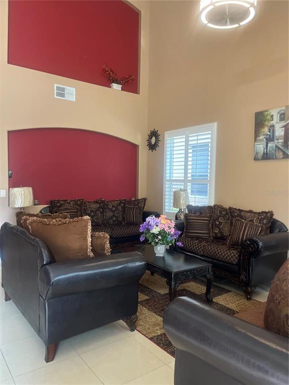 A living room features high ceilings, red accent walls, dark leather furniture, and tile flooring — 4015 LAKESIDE RESERVE LANE, ORLANDO, FL