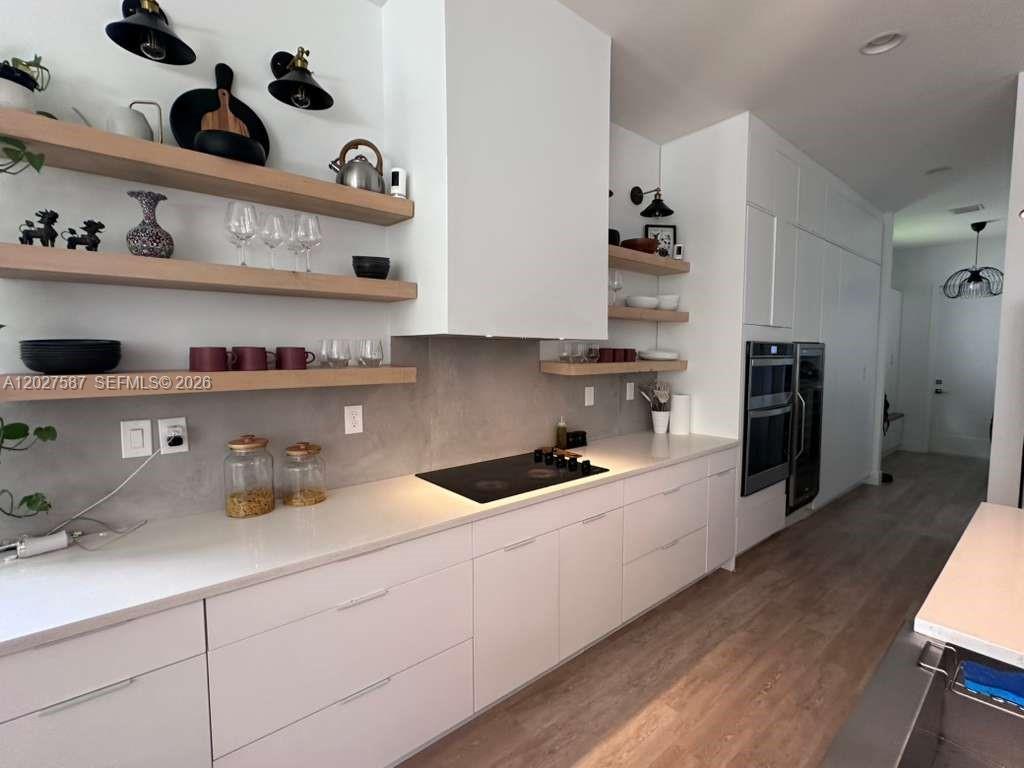 A modern kitchen features white cabinetry, light wood floating shelves, and a gray backsplash — 4572 SW 178th Ave, Miramar FL 33029, MIRAMAR, FL