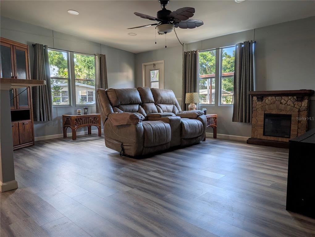 A living room features wood-look flooring, a central reclining sofa, and a stone fireplace — 7111 142ND AVENUE N Lot 101, LARGO, FL