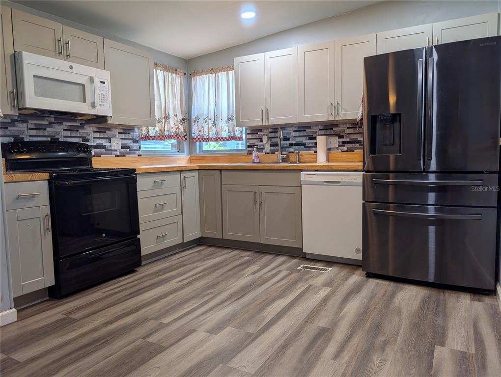 A kitchen features light gray cabinets, wood countertops, a black stove, and a stainless refrigerator — 7111 142ND AVENUE N Lot 101, LARGO, FL